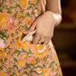 Summery mustard and peach floral sleeveless dress featuring a boat neckline and Hakoba pocket detailing, finished with soft off-white accents for a breezy, cheerful silhouette perfect for warm days.