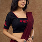 Timeless black blouse elevated by red intricate embroidery , adding a pop of colour .