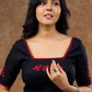 Timeless black blouse elevated by red intricate embroidery , adding a pop of colour .