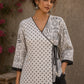 Black and white printed crossover top with contrast polka dots, lace-trimmed sleeves, side tie, tassels, and scalloped hem.