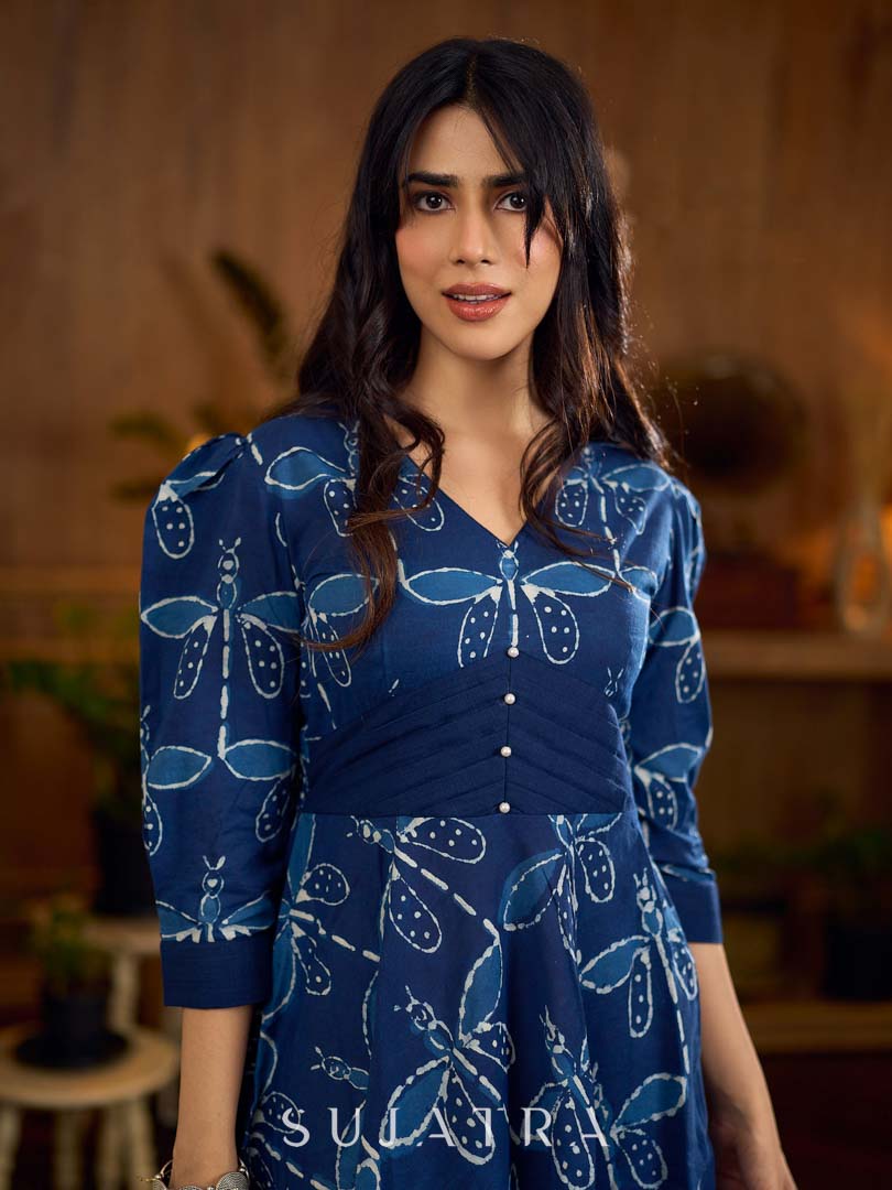 Indigo printed dress featuring dragonfly motifs, gathered sleeves with cuffs, and navy blue pleated waist detailing accented with pearls, creating a graceful silhouette with refined artisanal charm.