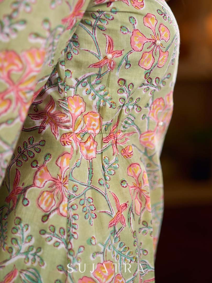 Soft green Gulmohar-printed dress featuring a square neckline and pearl-highlighted motifs, finished with an elasticated waist to create a flattering cinched silhouette with effortless charm.