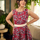 Red Gulmohar floral-printed sleeveless summer dress featuring off-white accents and scalloped lace detailing at the waist, creating a breezy, feminine silhouette perfect for warm, sunlit days.