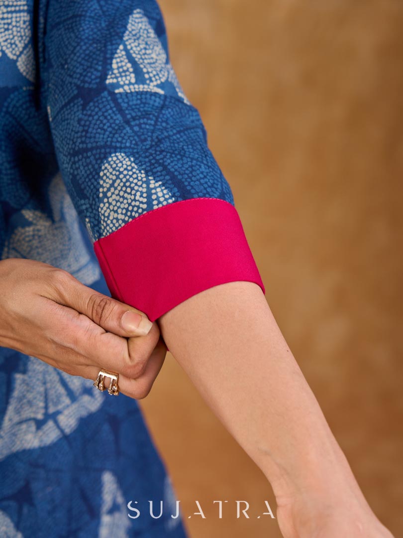 Deep indigo jacket with an asymmetric front closure, magenta folded cuffs, and coordinated accents, offering a structured silhouette with bold contrast and a refined look for elevated corporate styling.