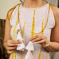 Sunlit ivory tie-dye dress with mustard accents and playful tassel shoulder detailing.