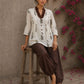 Off-white floral printed top with brown ruffled collar, button front, tie-up sleeves, tassel details, and contrast accents.
