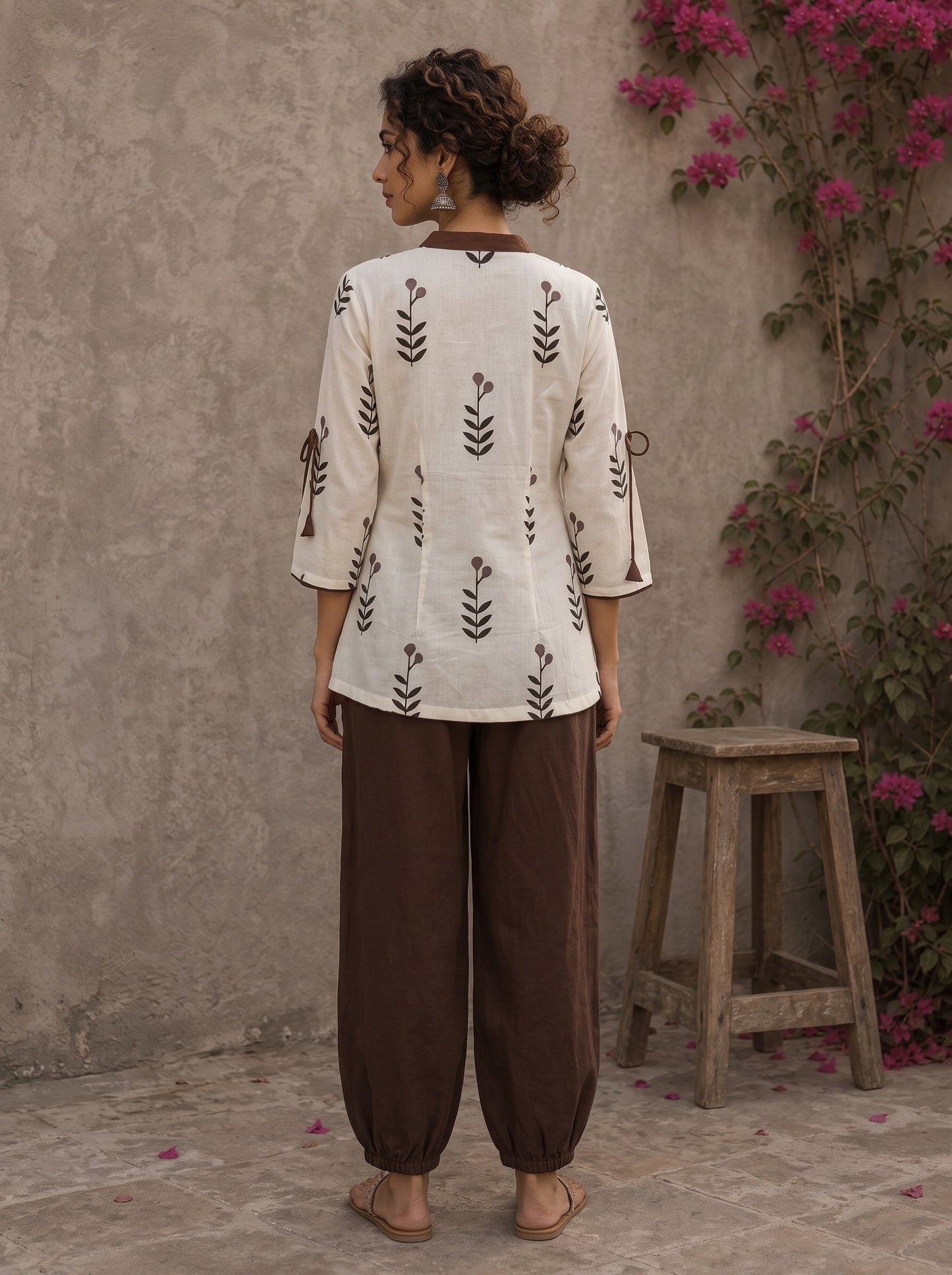 Off-white floral printed top with brown ruffled collar, button front, tie-up sleeves, tassel details, and contrast accents.