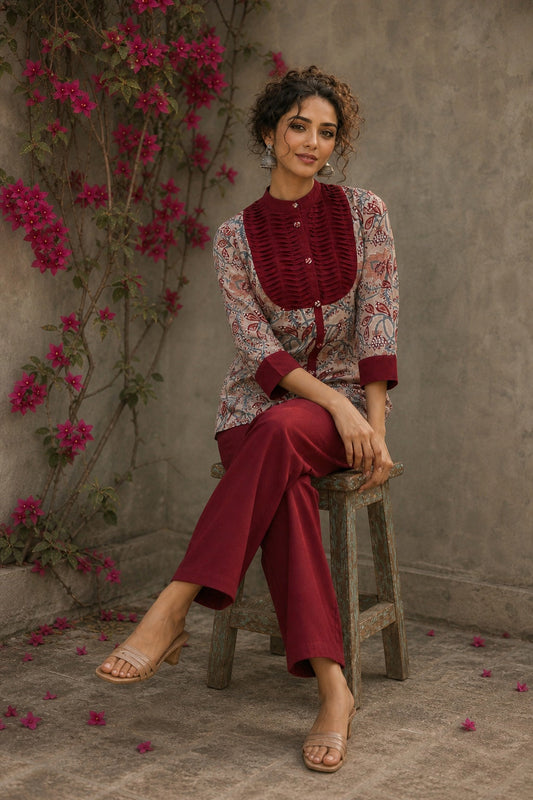 Elegant maroon floral top with intricate maroon pleats, high neckline, covered buttons, and coordinating sleeve cuffs.