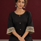 Elegant Black Cotton A-Line Dress with Madhubani Print Border Hem and Matching Bell Sleeve Cuffs — seated detail